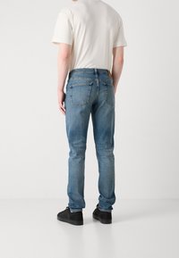 Ljusblå denimjeans med smal passform, fem fickor och sydda detaljer. Bärs med en ljus t-shirt och svarta skor.