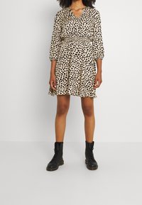 Leopard print dress in beige and black, with a V-neck, three-quarter puff sleeves, elasticized waist, and flared skirt. Black lace-up boots.
