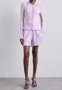 Lilac knitted cardigan with a collar and button closure, paired with matching sequined shorts. Accented with a fringed hem. Strappy silver heels.