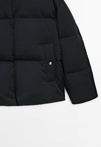 Black puffer jacket with a quilted design, featuring a side pocket secured with a silver snap button and a smooth, shiny texture.