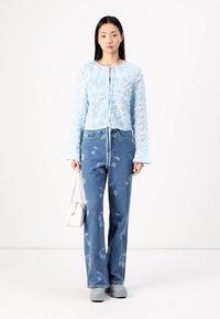 Light blue sheer blouse with textured floral pattern, paired with light blue denim jeans featuring a cherry design. Simple white handbag.