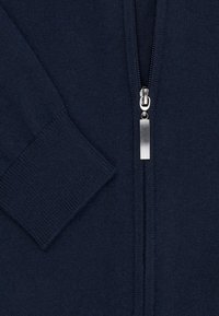 Granatowy kardigan na suwak z prążkowanymi mankietami i gładką fakturą. Metalowy suwak z prostokątnym uchwytem biegnie centralnie z przodu.