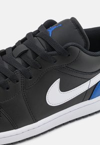 Crne kožne tenisice s bijelim Nike swoosh-om, plavim dodacima i crnim pertlama. Imaju teksturirani jezik i fleksibilnu gumenu potplatu.