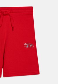 Röda bomullsshorts med elastisk midja och snörning, med detaljer i metallik på vänster sida. Lätt och avslappnad design.