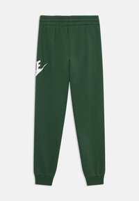 Calças de fato de treino verdes em algodão, com cintura elástica, tornozelos ajustados e um grande logotipo branco da Nike na coxa esquerda. Textura suave e ajuste descontraído.