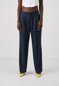 Pantalons rayés bleu marine avec une coupe décontractée, des plis et une taille élastique. Associés à des ballerines jaunes à angle, offrant des accents de couleur contrastés.