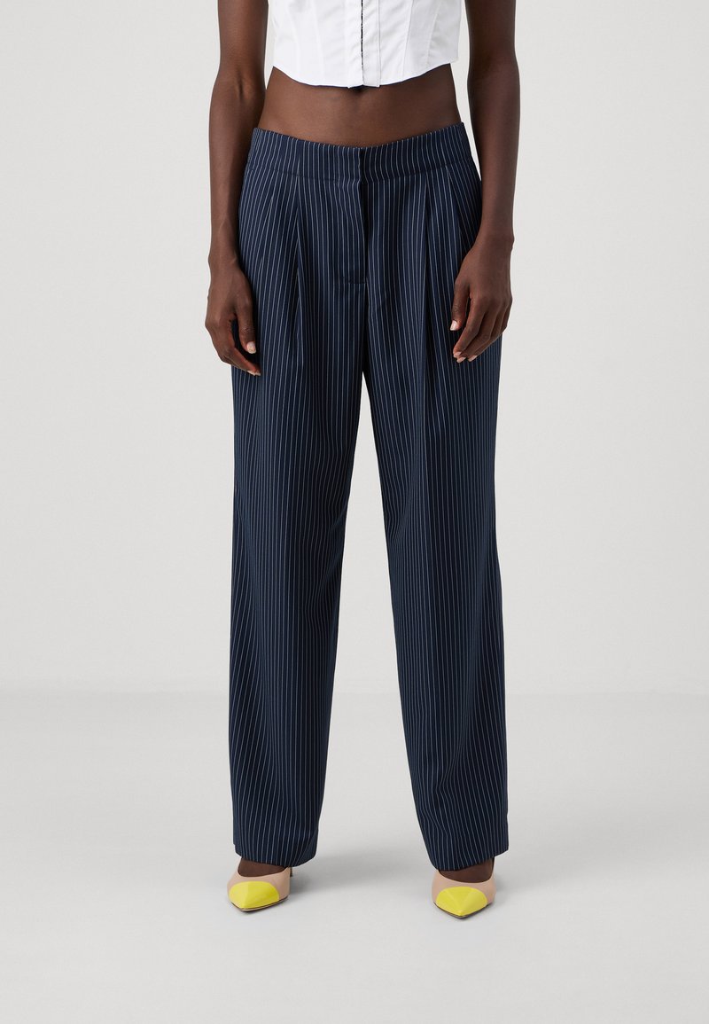 Pantalons rayés bleu marine avec une coupe décontractée, des plis et une taille élastique. Associés à des ballerines jaunes à angle, offrant des accents de couleur contrastés.