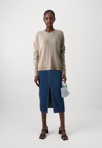 Beiger gerippter Pullover, Jeans-Bleistiftrock mit vorderem Schlitz, schwarze Blockabsatzsandalen, kleine hellblaue Handtasche. Glatte und strukturierte Textilien.