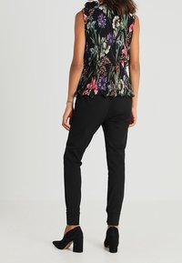 Blusa senza maniche con motivo floreale e orlo peplum, abbinata a pantaloni neri a sigaretta e scarpe con tacco nere, vista da dietro.