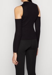 Czarna, żeberkowana bluzka z długim rękawem, z wycięciem na ramionach, wysokim kołnierzem i dopasowanym krojem, wykonana z elastycznego materiału dzianinowego.
