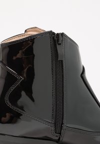 Stivale alla caviglia in pelle verniciata nera con zip laterale e design elegante, caratterizzato da una texture liscia e lucida e dettagli di cucitura minimi.