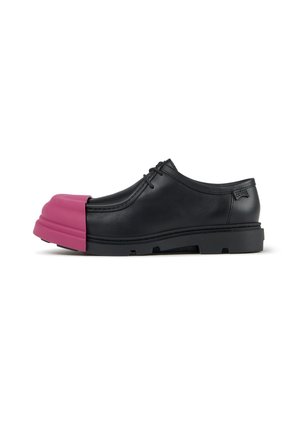 Zapato de vestir de cuero negro con cordones y suela gruesa, con una gran cubierta protectora de goma de color rosa brillante sobre la zona de los dedos.