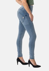 Vaqueros ajustados azul denim con cintura alta, sutiles desgastes y bolsillos traseros, combinados con tacones negros de punta afilada.