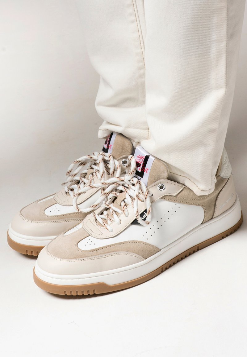Beige and white sneakers with suede and leather textures, featuring perforated detailing, patterned laces, and gum rubber soles.