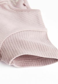 Light pink ribbed fabric with a smooth texture, showing a hemmed edge and slight stretch. The design features a close-fit round neckline.