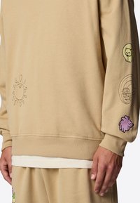 Beige sweatshirt i bomull, med ribbad mudd och nederkant. Dekorerad med fantasifulla broderade mönster på bröstet och ärmarna.