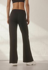 Black flared pants made of stretchy fabric, featuring a high waistband and a smooth texture, paired with white athletic shoes.