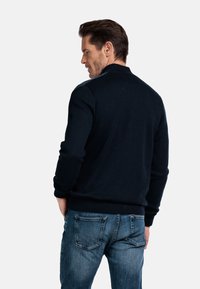 Navyblauwe gebreide trui met een hoge kraag, geribde manchetten en zoom. Gecombineerd met lichtblauwe denim jeans. Katoenmix stof.