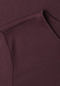 Close-up of a maroon knitted fabric showing the shoulder seam and V-neck collar stitching.