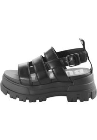 Black platform sandal made of smooth leather, featuring three wide straps, a buckle closure, and a textured rubber sole.