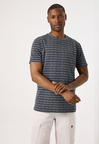 Camiseta de manga corta en azul marino con rayas horizontales blancas y un pequeño logo en el lado izquierdo del pecho. Tela de algodón con una textura suave.