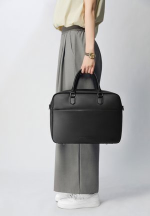 Valigetta in pelle nera con doppio manico, forma rettangolare e texture liscia. Presenta una tasca frontale e un logo discreto sul fondo.