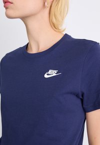 T-shirt en coton bleu marine à manches courtes, avec un logo Nike blanc brodé sur le côté gauche de la poitrine. Texture lisse.