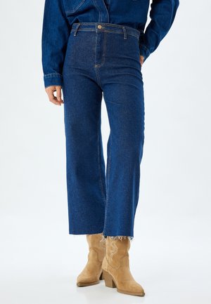 Pantalones vaqueros de mezclilla azules de cintura alta, acampanados en la parte inferior, con un dobladillo deshilachado y un diseño clásico de cinco bolsillos con detalles de costura sutiles.