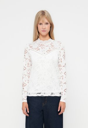 White lace top with long sleeves, featuring floral patterns, a rounded neckline, and a fitted silhouette, paired with dark denim bottoms.