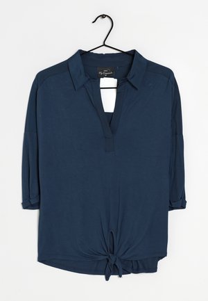 Granatowa koszula z kołnierzykiem i głębokim dekoltem w kształcie litery V, z rękawami do trzech czwartej oraz zawiązanym detalem na dole. Miękka tekstura tkaniny.