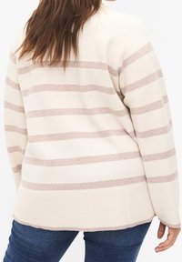 Maglione crema con strisce orizzontali marroni chiari, orlo a coste e vestibilità leggermente ampia. Abbinato a jeans di denim scuri visibili nella parte inferiore.