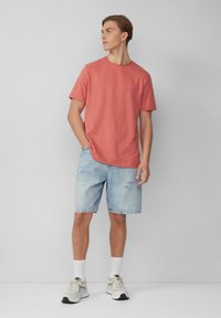 Koraalkleurig T-shirt met korte mouwen, lichtblauwe distressed denim shorts, witte sokken en grijze sneakers. Eenvoudig ontwerp met een relaxte pasvorm.