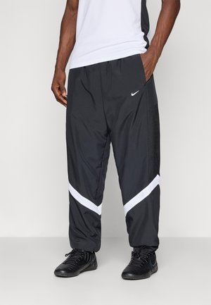 Black athletic pants with white side stripes, made of lightweight fabric. Features mesh panels for breathability. Paired with black shoes.