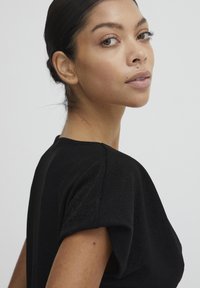 Top nero a maniche corte con un design strutturato e una leggera lucentezza. Presenta un collo rotondo e una texture liscia, che esalta le spalle.
