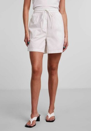 Pantaloncini di cotone bianco con vita elastica e coulisse. Presentano una vestibilità ampia e tasche laterali. Indossati con sandali bianchi con cinturini.