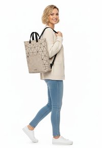 Beige ryggsäck med geometriskt mönster, texturerad framficka, dubbla svarta remmar, rektangulär form och minimalistisk design.