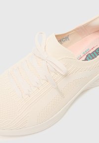 Helle beiger Sneaker mit einem gestrickten Obermaterial, runder Zehenpartie, strukturierten Seiten und flachen Schnürsenkeln, ausgestattet mit einer weichen rosa Innensohle für zusätzlichen Komfort.