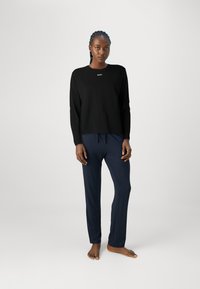 Svart långärmad topp med en liten "BOSS"-logotyp, matchad med marinblå elastiska midjebyxor. Materialet verkar mjukt och lätt.