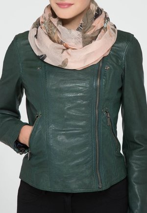 Femme portant une veste en cuir vert foncé avec une fermeture éclair frontale et des poches verticales zippées, associée à une écharpe légère rose pâle à motif floral.
