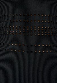 Černá žebrovaná tkanina s vodorovnými řadami malých, kulatých výřezů. Povrch je hladký, což zdůrazňuje jednotný vzor a tvar.