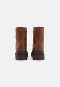 Brune lær ankle boots med en teksturert finish, glidelås på siden og en tykk, mørk såle. Minimalistisk design med gull detaljer.