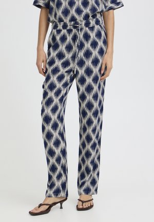 Granatowo-białe spodnie na sznurki w wzory noszone z dopasowanym topem i brązowymi sandałami na obcasie na stojącej osobie.