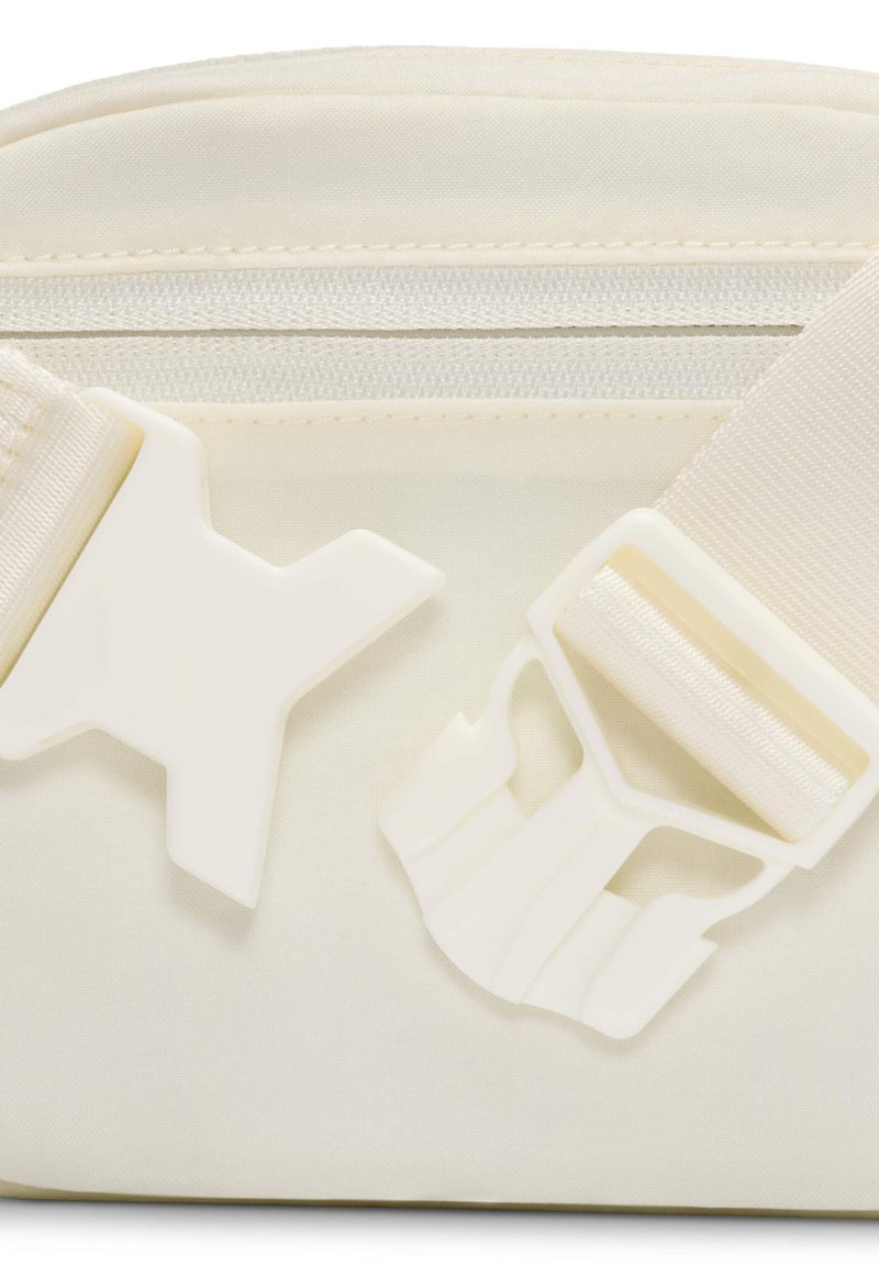 Primo piano di una borsa in tessuto color avorio con fibbia laterale in plastica a sgancio rapido e dettaglio di cerniera su tracolla regolabile.