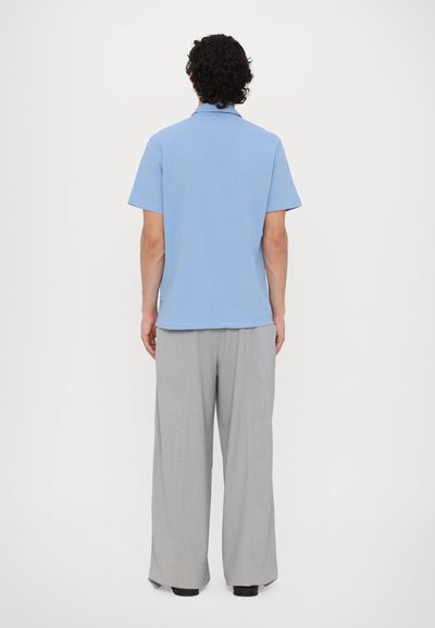 Polo azzurro chiaro a maniche corte con colletto, abbinato a pantaloni larghi grigi chiari. Tessuto morbido e vestibilità comoda.