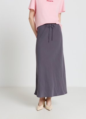 Persona che indossa una camicia rosa a maniche corte e una lunga gonna grigia con coulisse, abbinata a scarpe beige con tacchi alti.