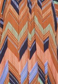 Tessuto multicolore a fantasia con design a zigzag chevron in tonalità di marrone, blu navy e pastello. Texture caratterizzata da accenti a pois in tutto il tessuto.