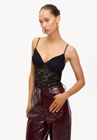 Zwarte kanten body met dunne bandjes, voorzien van een bloemenpatroon, gecombineerd met hoge maroon nepleer broek met een glanzende afwerking.