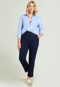 Camisa de botones de rayas azul claro, combinada con pantalones azul marino oscuro. El modelo lleva zapatillas metálicas. Telas suaves, diseño a medida.