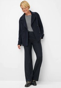 Navy wollen dubbelzijdig jasje over een gestreepte zwart-witte top, gecombineerd met donkere broeken en zwarte instappers met gouden accenten.