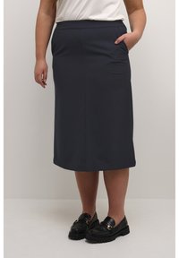 Tmavomodrá midi sukňa z hladkého materiálu, s vysokým pásom, bočnými vreckami a rovnou siluetou, v kombinácii s čiernymi loafers.